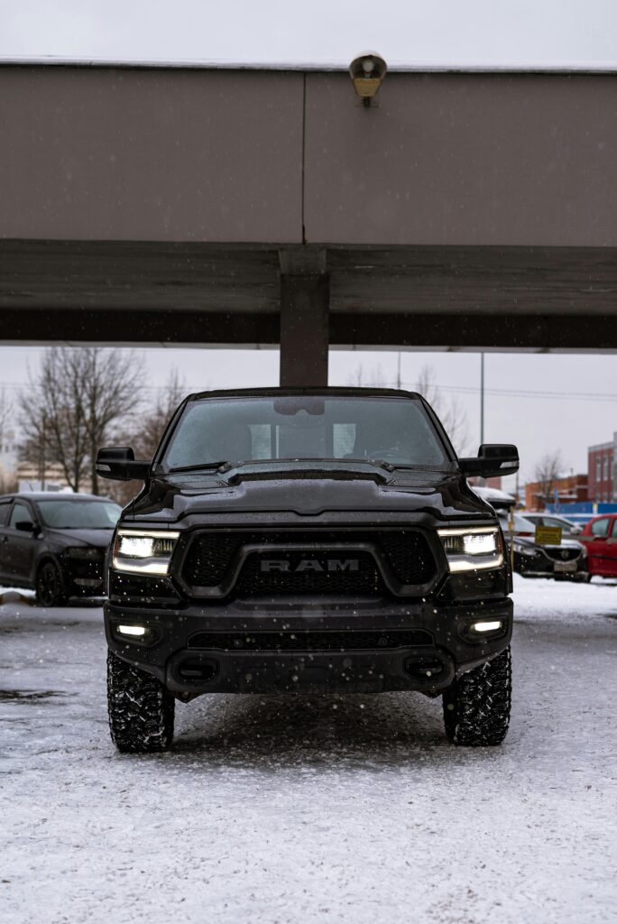 Front view of a black Dodge Ram 1500 Rebel parked under a bridge in a snowy urban area.